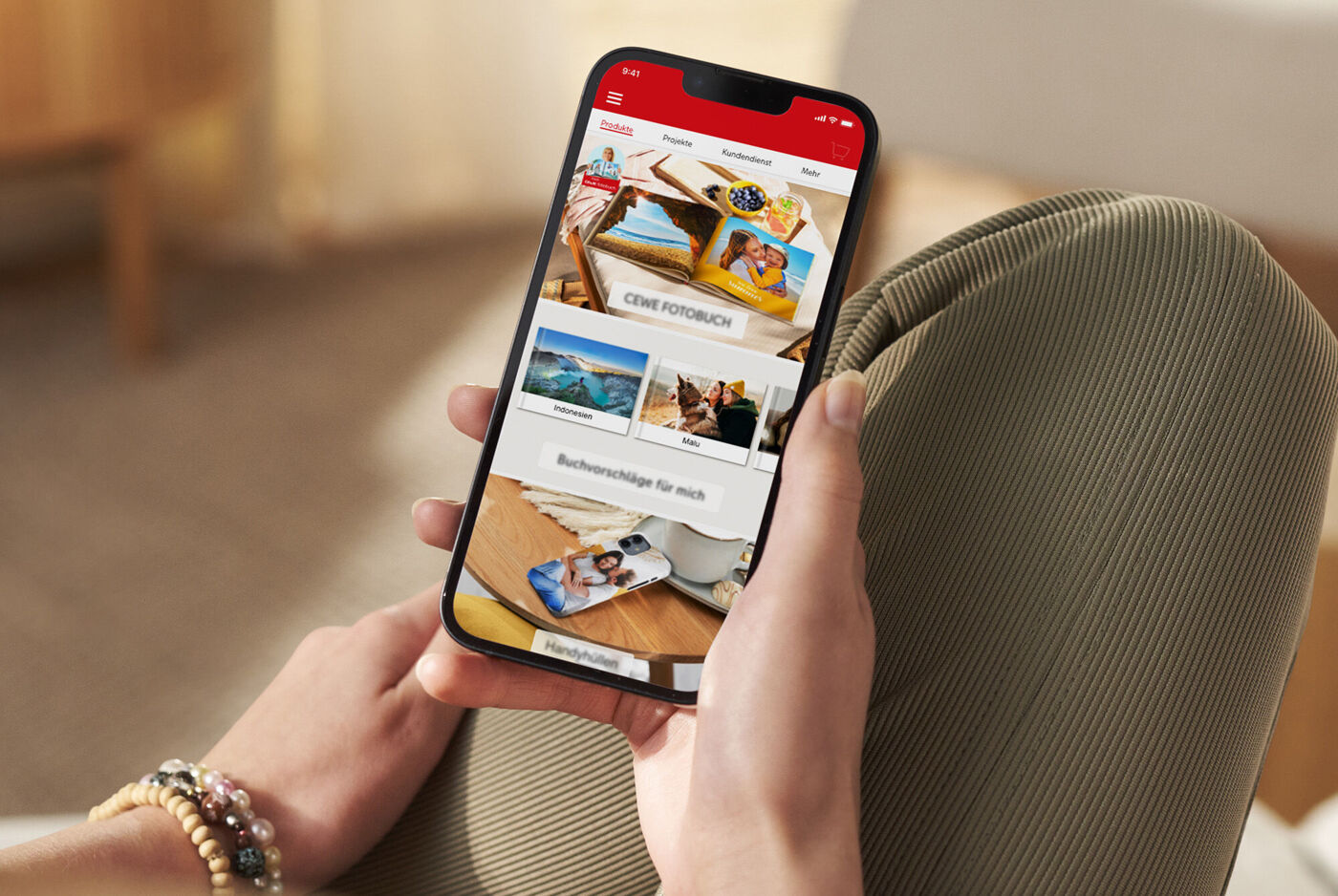 Person holder smartphone med CEWE-app, viser fotobøger.